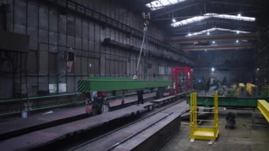 Metal kiriş fabrikada zincirlerle taşınır. Şarjör. Zincirlere asılmış çelik kiriş fabrikada sürüklenir. Zincirlerdeki askıdaki kiriş fabrikanın etrafında hareket ediyor