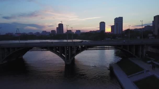Luchtfoto van de rivier en het stadsgezicht op de achtergrond van de bewolkte zonsondergang. Voorraadbeelden. Verschillende gebouwen van een stad, concept van natuur en verstedelijking. — Stockvideo