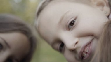 Bulanık yeşil ağaçların arka planındaki kameraya bakıp gülümseyen komik küçük kızların yüzlerini kapatın. Başla. Mutlu çocukluk kavramı.