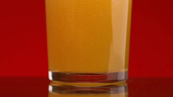 Öl hälls i genomskinligt glas på isolerad bakgrund. Lagerbilder. Lätt öl med skum hälls i glas på röd bakgrund. Karbonerad gul dryck i glas. Skadliga kolsyrade drycker — Stockfoto