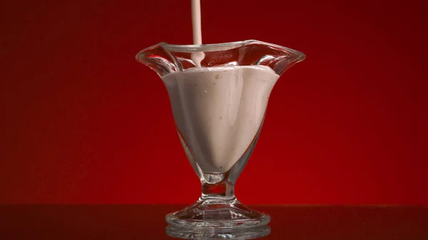 Close-up de iogurte em copo de vidro no fundo vermelho. Imagens de stock. Iogurte fresco é derramado em vidro transparente. Fluxo de smoothies enche vidro em fundo isolado — Fotografia de Stock