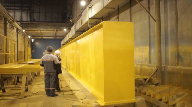 Fabrikadaki boya bölümü. Şarjör. İşçi boyalı yüzeyi elle kontrol ediyor. Büyük metal parçası fabrikada boyanıyor. Büyük ekipmanların boyalı parçaları
