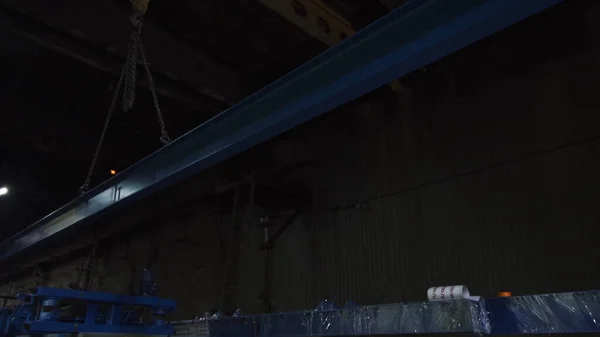 Metal beam is moved on chains in factory. Clip. Steel beam suspended on chains is dragged at factory. Suspended beam on chains moves around factory