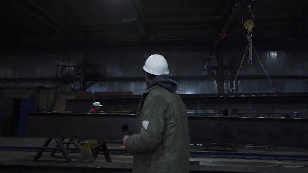 El hombre camina por la fábrica y mira a su alrededor. Clip. Foreman supervisa el trabajo y la producción de todas las partes de la planta. Ingeniero o capataz supervisa la producción en fábrica — Foto de Stock