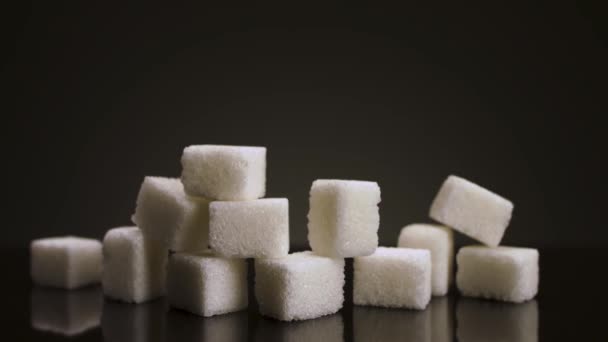 Stos kawałków cukru na czarnym tle. Materiał filmowy. Zbliżenie słodkiego cukru jako symbolu chorób i otyłości. — Wideo stockowe