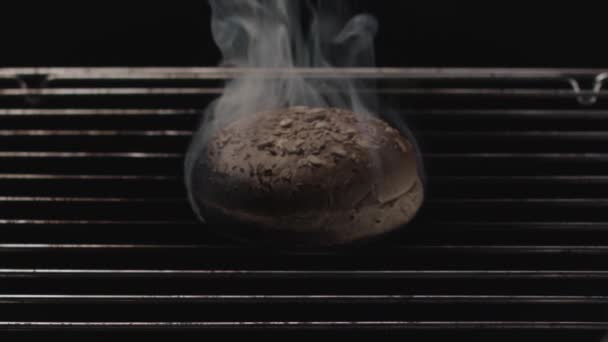 Zblízka spálený chléb uvnitř trouby s kovovými mřížemi na černém pozadí. Záběry ze skladu. Přepečený hamburger a stoupající kouř. — Stock video