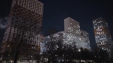 Gece gökyüzünün arka planında güzel konutlar var. Başla. Geceleri parlayan pencereleri olan çok katlı binaların alt manzarası