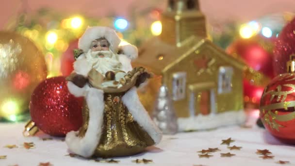 Різдвяні та новорічні прикраси, дитячі іграшки Отець Мороз та золотий будинок. Концепція. Замкнуті мордою, що блимає, і прекрасна композиція з іграшками, конфетті, білою сніжно - білою тканиною і сяючою. — стокове відео