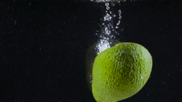 L'avocado cade in acqua. Azione. Rinfrescante avocado maturo cade in acqua con bolle su sfondo nero. L'avocado fresco è immerso in acqua — Video Stock