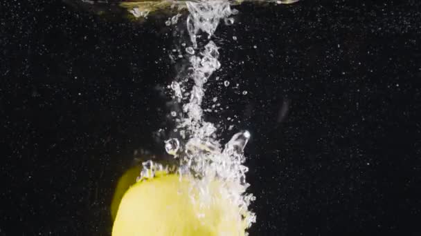 Primo piano di limone intero che cade in acqua. Azione. Limone intero cade in acqua con bolle su sfondo nero. Rinfrescante gocce di limone in acqua — Video Stock