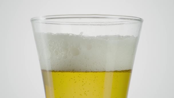 Close-up de cerveja em vidro transparente sobre fundo branco. Acção. Cerveja em vidro com espuma desaparecendo em fundo isolado. A espuma na cerveja lentamente desaparece — Vídeo de Stock