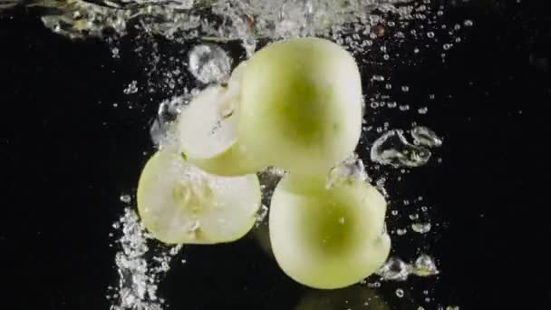 Metà delle mele verdi in acqua. Azione. Succose mele verdi cadono in acqua con bolle su sfondo nero. Acqua rinfrescante con mele verdi — Video Stock