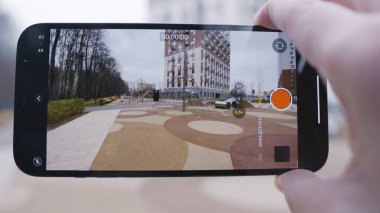 Telefonun video çektiği ekrana yakın çekim. Başla. Adam telefonu tutuyor ve oyun parkı ve çok katlı binanın videosunu çekiyor.