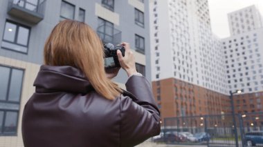 Kadın profesyonel kameralı binaların fotoğraflarını çekiyor. Başla. Güzel kadın fotoğrafçı çok katlı binaları çekiyor. Konut binalarının arka planında kadın fotoğrafçının arka görüntüsü