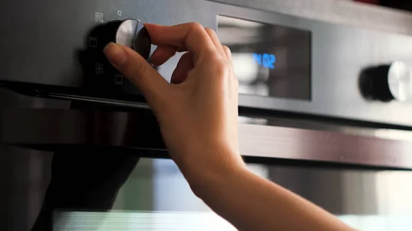 Woman twisting the handle of a modern oven. Concept. Details of cooking at the kitchen, adjusting temperature of a stove.