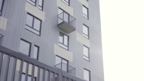 Exterior de un nuevo edificio de apartamentos y cerca de hierro negro. Acción. Vista inferior de una fachada de casa de varios pisos con ventanas y balcones. — Vídeos de Stock