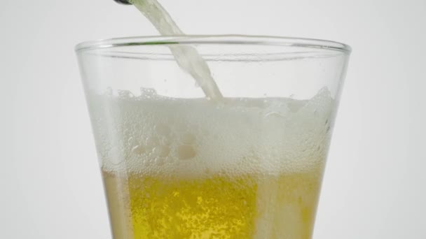 Close-up of beer being poured into clear glass. Action. Beer is poured into transparent glass on white isolated background. Beer is poured into glass — Stock Video