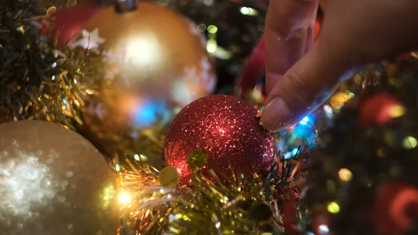 Close up of girl hand taking a red plastic shining Christmas ball. Concept. New Year holidays, toys and garland for spruce decoration. — Stock Photo, Image