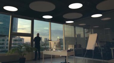 New York, ABD - 08.29.2020: Ofisindeki uzun panoramik pencerenin yanında duran bir iş adamının arka görüntüsü. Stok görüntüleri. Apple Mac bilgisayarı modern bir ofis binasının içinde masanın üzerinde duruyor..