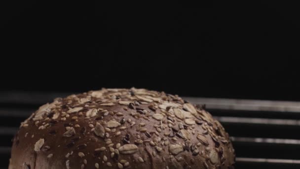 Primo piano di pane rotondo fatto in casa a forma di pane cotto nel forno a fuoco aperto. Filmati delle scorte. Pane integrale con semi e cereali su fondo nero. — Video Stock