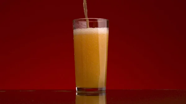 Orangensaft in ein Glas auf rotem Hintergrund gießen. Archivmaterial. Konzept der gesunden Ernährung, Vitamin C und Immunität. — Stockfoto