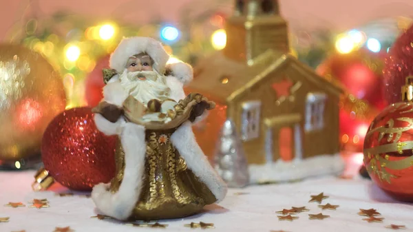Noel ve yeni yıl süslemeleri, çocuk oyuncakları Peder Frost ve altın bir ev. Kavram. Yanıp sönen çelenk ve güzel kompozisyon oyuncaklar, konfeti, beyaz karlı kumaş ve parlayan — Stok fotoğraf