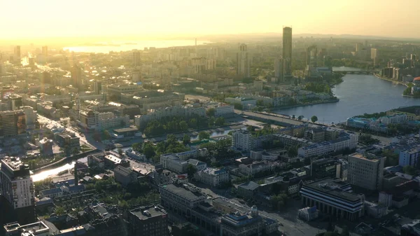 Aerial view of skyscraper, beautiful city during sunset and the river. Stock footage. Golden sky above the houses and streets. — Stock Photo, Image