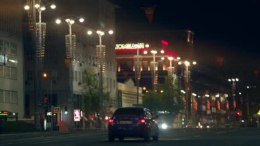 Akşamları hareket halindeki araçlarla sokak manzarası. Stok görüntüleri. Dekoratif sokak fenerlerinin ve kara gökyüzü arka planındaki binaların gece görüşü.