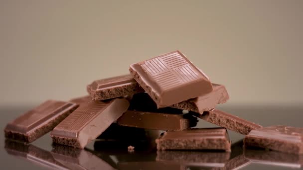 Close up of milk tasty chocolate pieces lying on the table. Stock footage. Broken chocolate bar isolated on beige background, concept of sweets and confectionary. — Stock Video