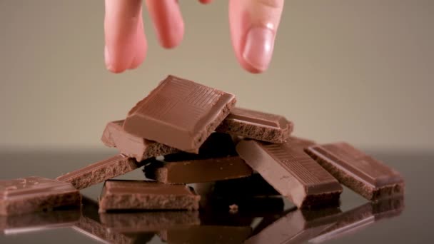 Gros plan de la main en prenant un morceau de chocolat savoureux au lait couché sur la table. Images d'archives. Barre de chocolat cassée isolée sur fond beige, concept de bonbons et confiseries. — Video