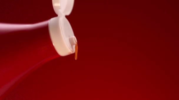 Le ketchup de tomate est pressé dans une bouteille rouge avec couvercle blanc. Images d'archives. Gros plan d'une goutte de sauce tomate tombant de la bouteille isolée sur fond rouge. — Video