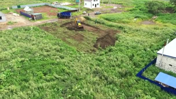 Aerial view of the beginning of new house construction. Clip. Tractor is dogging a hole for the house foundation in the countryside area. — Stock Video