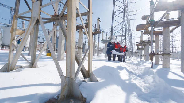 Engineers at electrical substation in winter. Action. Engineers and electricians look at electrical substation plan in winter. Working electrical substation on clear winter day