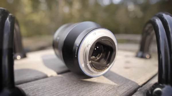 Close up of camera lens lying on rotating children roundabout on green blurred trees background. Action. New camera lens is forgotten on children playground. — Stock Photo, Image