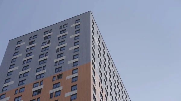 Hochhaus-Apartmenthaus umgeben von blauem Himmel. Handeln. Neu gebautes mehrstöckiges Wohnhaus in grauen und orangen Farben. — Stockfoto