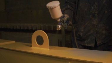 Adam boya spreyiyle büyük metal bir detayı sarıya boyuyor. Şarjör. Fabrikada boyama, metal yapıların sprey boyası..