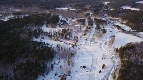 Drone widok z lotu ptaka tradycyjnej wsi wsi położonej w cichym miejscu ze świeżym powietrzem i lasem. Akcja. Zimowy krajobraz z małymi domkami na śniegu, drodze, drzewach i niebieskim, zachmurzonym niebie. — Wideo stockowe