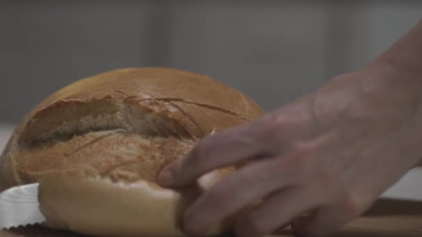 Крупним планом жіночі руки нарізають білий хліб повільним рухом на дерев'яній дошці. Дія. Різання свіжоспеченого круглої форми буханця білого хліба зі сталевим ножем . — стокове відео