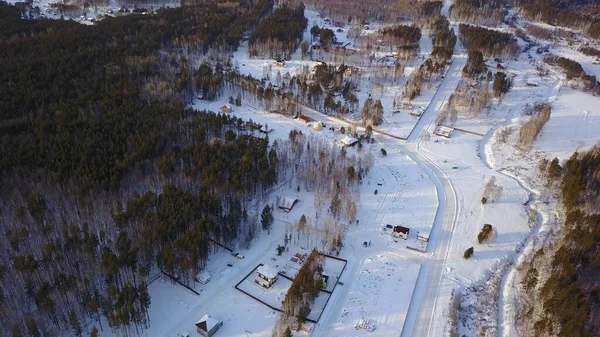 Casas de pueblo clásicas y las calles cubiertas de nieve fresca profunda en invierno, vista aérea. Acción. Pequeño asentamiento situado cerca del bosque de pinos en un día soleado. — Foto de Stock