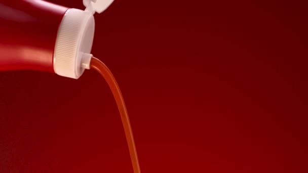 Tomato ketchup is squeezed from a red bottle with white lid. Stock footage. Close up of pouring tomato sauce from the bottle isolated on red background. — Stock Video