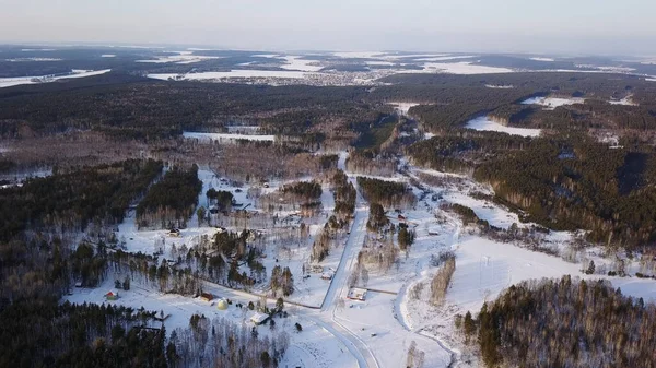 Klassieke dorpshuizen en de straten bedekt met diepe verse sneeuw in de winter, vanuit de lucht. Actie. Kleine nederzetting gelegen nabij dennenbos op een zonnige dag. — Stockfoto