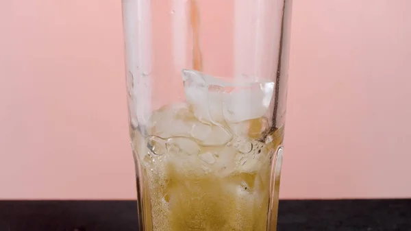 Llenado de vidrio con agua de soda con hielo. Acción. Primer plano de verter refresco con muchas burbujas dentro del vidrio transparente aislado sobre fondo rosa. —  Fotos de Stock