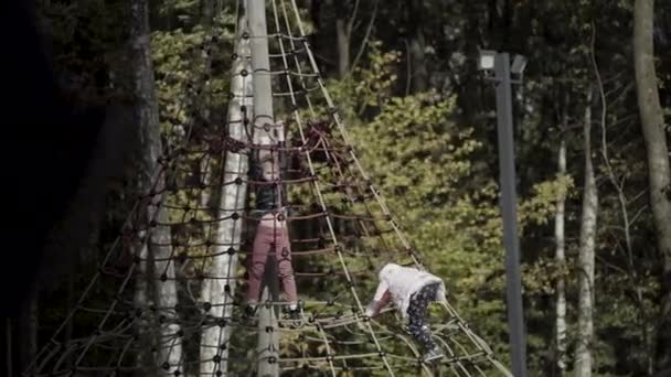 Raparigas felizes a brincar no parque infantil. Acção. Crianças se divertindo com a rede de escalada ao ar livre perto de floresta verde no início do outono. — Vídeo de Stock