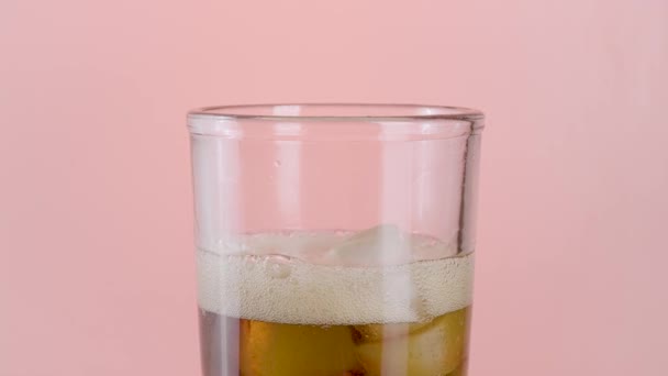Närbild av ett glas med läsk vatten och isbitar. Börja. En mjuk dryck med många bubblor inuti transparent glas isolerad på rosa bakgrund. — Stockvideo