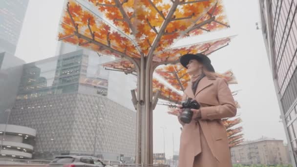 A nő őszi várost fényképez. Felvétel. Gyönyörű nő készít képeket városi tájak ősszel professzionális fényképezőgéppel. Női fotós képeket készít a városról a felhős esős napokon — Stock videók