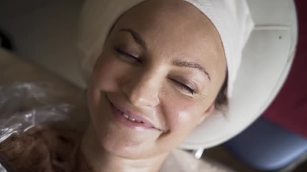 Una mujer tumbada en la cama y relajada en el salón de spa. Acción. Vista superior de la cara femenina relajada y sonriente con una máscara de chocolate en su cuerpo en el estudio de belleza. — Vídeos de Stock