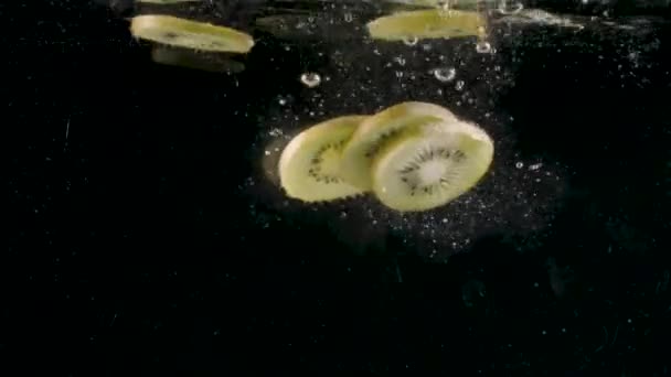Fatias de frutas kiwi cair na água cheia de bolhas em câmera lenta. Acção. Close up de frutas tropicais cortadas caindo subaquático isolado em fundo preto. — Vídeo de Stock