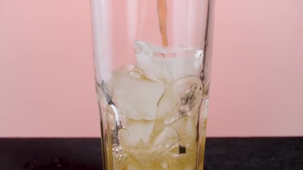 Fyllning glas med läsk vatten med isbitar. Börja. Närbild av hälla läsk med många bubblor inuti transparent glas isolerad på rosa bakgrund. — Stockvideo