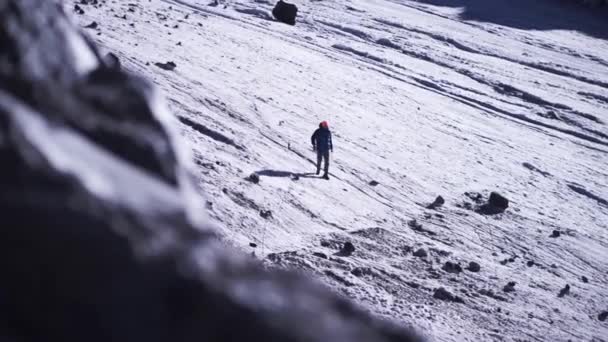 ein Mann, der an einem sonnigen Wintertag am schneebedeckten Berghang spaziert. clip. Wandern in den Bergen, Konzept des aktiven Lebensstils. 
