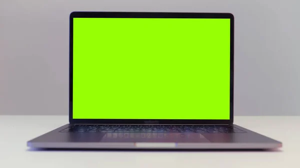 Modern dizüstü bilgisayarın krom anahtarlı yeşil ekranı beyaz duvar arka planında duran bir masanın üzerinde yakın plan görüntüsü. Başla. Uzaktan çalışma ve teknoloji kavramı.